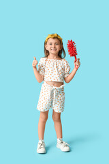 Cute little happy girl with bottle of detergent and brush showing thumb-up gesture on blue background