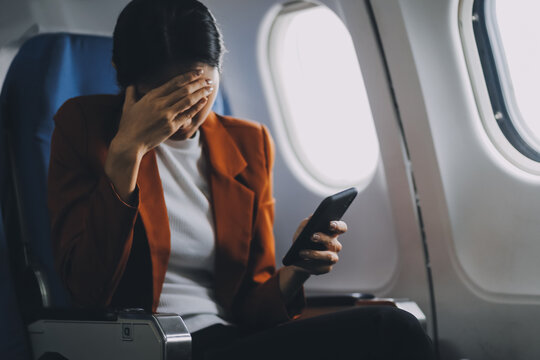 Stressed and serious young asian businesswoman remote working on the plane, suffering from headache and airsick during the flight.