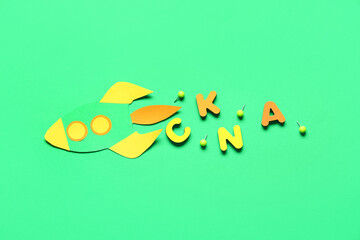 Paper rocket with pins and wooden letters on green background