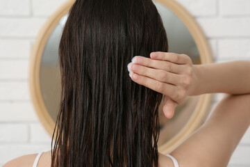 Fototapeta premium Beautiful young woman applying hair mask in bathroom, back view