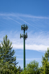 Mobile telecommunications cell site with monopole tower and antennas painted green against a blue sky with wispy white clouds on a sunny summer day
