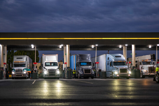 Big rig semi trucks with semi trailers filling truck tanks at a gas station on a truck stop at night time