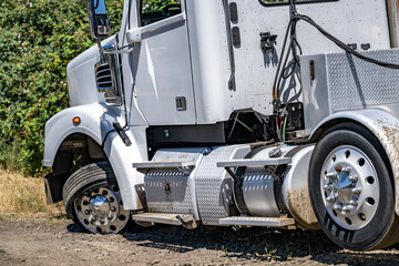 Broken down white big rig semi truck with a twisted wheel and a punctured tire standing out of...