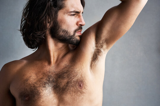 Studio, sweat and man smelling underarm for grooming, skincare and poor hygiene in wellness treatment. Stink, skin and male model with strong body odor, bacteria and dirty armpit on grey background