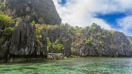 Picturesque karst rocks with steep slopes and sharp peaks surround the turquoise lagoon. Green...