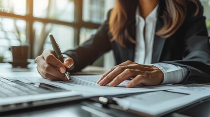 Business professional writing notes in an office, showcasing productivity and focus on paperwork with a laptop.