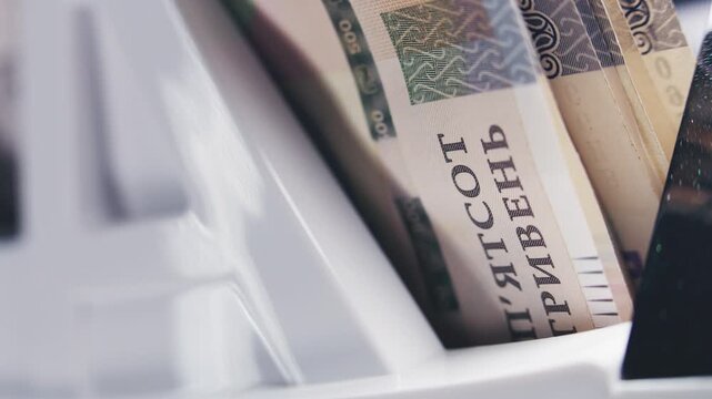 Money counting machine counts five hundred hryvnia banknotes for currency exchange or payment. Automatic cash counting equipment. Ukrainian money bills. Finance, inflation and banking. Close Up.