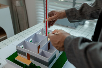 Obraz premium An architect works in the office, an engineer is using a tool to take measurements of a house model so that it matches the blueprint, there is a house model on the architect's desk