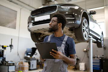 Auto mechanic holding clipboard checking car repair in service workshop. Professional technician...