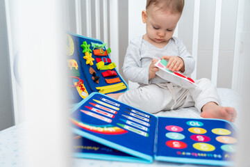 Baby playing with felt busy book sitting in crib. Concept of smart books and modern toys