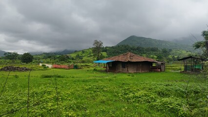 A charming hut set in green fields, with monsoon rains and mountains visible, capturing the essence...
