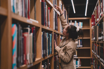 In the university library, a young female student immersed in her studies is carefully choosing literature, embodying the essence of education and the pursuit of knowledge indoors.