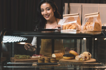 portraits of waitress looking at bakery and choose a bread for customer order. the happiness woman in bakery shop on waiter uniform and service customer.