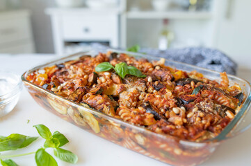 Delicious vegetarian pasta casserole with mediterranean vegetables, whole wheat noodles , parmesan cheese and pine nuts on kitchen counter.