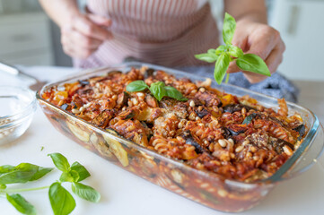 Woman putting a basil leaf on a fresh and homemade baked vegetarian pasta casserole