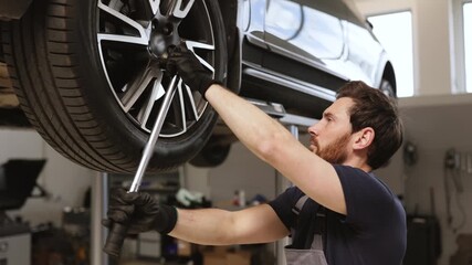 Mechanic smiling while working on car in auto repair shop. Vehicle elevated on lift, professional tools and equipment in background. Concept of automotive maintenance, technical expertise.