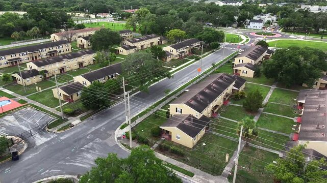 Aerial flyover housing area with row of houses in suburb of Orlando City, Florida. Yellow facade and black roofs. Roundabout in background. Wide shot.