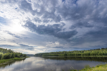 A wide shot of a river winding through a verdant valley, with a dramatic sky filled with storm clouds above.