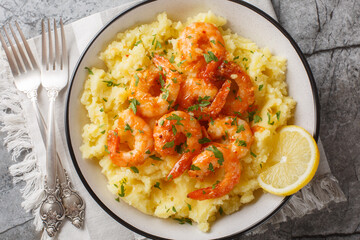 Fried garlic shrimps served with hot mashed potatoes, lemon and herbs close-up in a bowl on the table. Horizontal top view from above