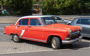 An aged red sedan with a white roof is parked on a city street. The car has a number seven painted...