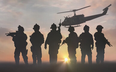 silhouette of military special force unit with helicopter in the background under sunset sky