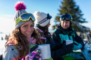 Friends enjoying a sunny winter day on the mountain, sipping tea and basking in the snowy...