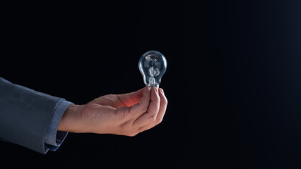 Close-up. Businessman in suit holding lightbulb against dark background, symbolizing ideas innovation.combination of brainstorming, contemplation, imagination, leveraged our intelligence to develop
