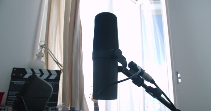 Beautiful slow motion shot of a famous Shure brand microphone ready to use for a podcast in a home studio with dim light coming in through the balcony.