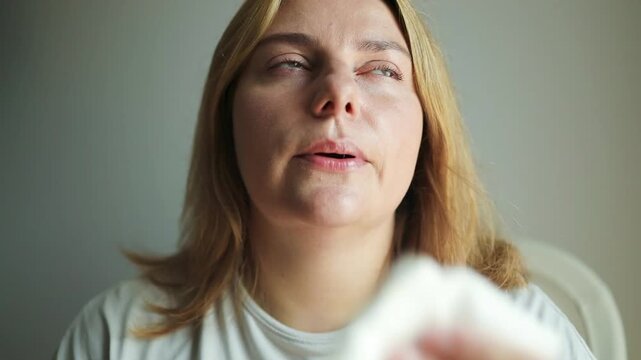 Young woman having hot flash and sweating in a warm summer day at home. Woman drying with paper napkin in too hot weather. High quality FullHD footage