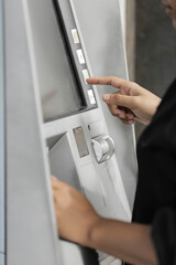 young woman withdrawing money with credit card from ATM machine typing pin code 