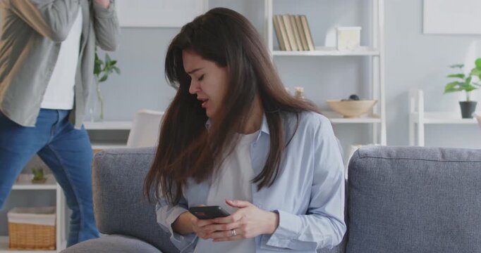 Woman is frantically trying to dial number on mobile phone when angry man snatches phone from hands. Panicked woman tries to find help on phone, while man nervously shakes his hands in background.