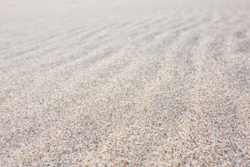 Close-up of light sand on a beach with longitudinal irregularities created by the wind. There are individual black grains of sand on the surface. Background. Texture