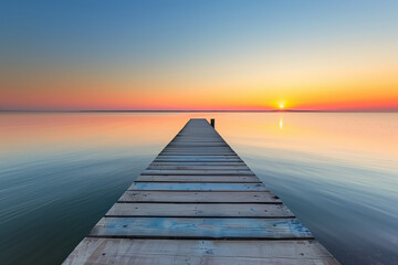 Obraz premium Beautiful seascape long jetty pier at sunset. Minimal sea sky, calm water surface and reflections. Colorful peaceful sunrise tones orange, gold, blue. Tranquil relaxing panoramic inspire meditation