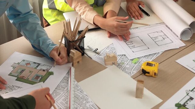Smart architect and safety engineer discussion about building blueprint on table with architectural document, measurement tools and wooden block scatter around at modern office. Closeup. Delineation.