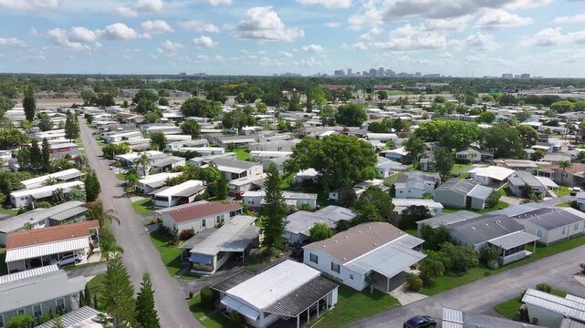 Extensive mobile home park with tree-lined streets in Florida. Numerous trailers with green spaces and distant city skyline. Aerial.