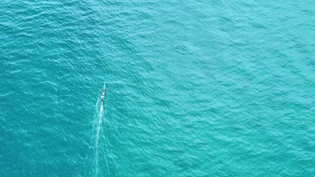 Fishing boat sailing over a coral reef in the crystal clear water of the ocean aerial view