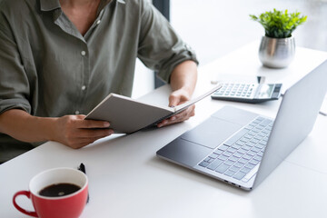 Businesswoman sitting at desk on couch in workplace or at home working on laptop and analyzing data on charts and graphs and writing on papers to make business plan and strategies for company, 