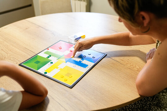 Mother and son strategizing on a Parcheesi board, focused on the game.