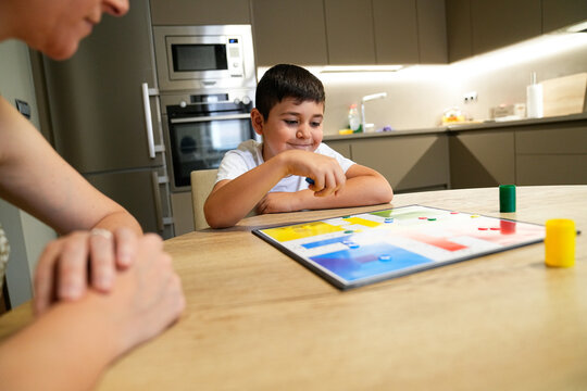 Boy smiling while moving a piece during a board game with mother