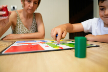 Fototapeta premium Boy moving a game piece with mother watching closely