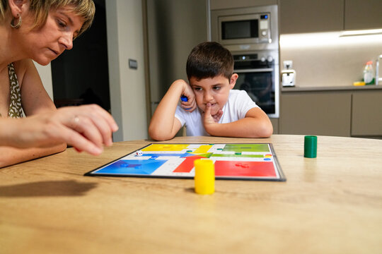Boy and mother focusing on a board game move at the kitchen table