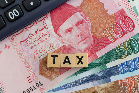 Wooden blocks TAX word on Pakistani banknotes with calculator. Tax concept.