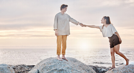 Couple, beach and holding hands for love on rock, support and outdoor romance in relationship. Happy people, holiday ocean and nature in marriage, together and travel for peace by sea for affection