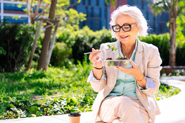 middle age entrepreneur woman eating a takeaway salad sitting outdoors in a city park, concept of healthy food and active lifestyle in adulthood, copyspace for text