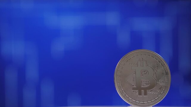Close-up of a silver bitcoin coin slowly spinning on a digital blue background. Digital money, banking, investment, finance and business concept.