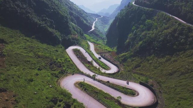 This footage captures the breathtaking winding road through the lush green mountains of Ha Giang, North Vietnam. The shot highlights the dramatic curves of the road as vehicles navigate it.