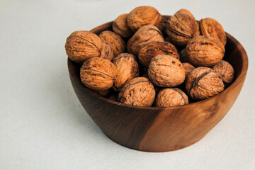 Unpeeled walnuts in a wooden bowl on a gray background. Autumn background. Top view