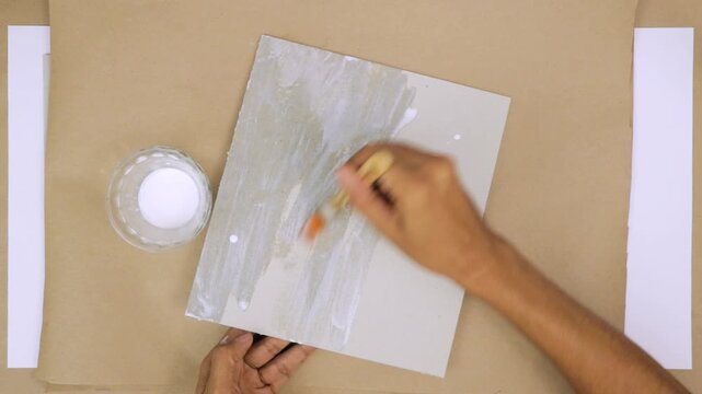 A person applying bookbinding glue to gray cardboard with a brush