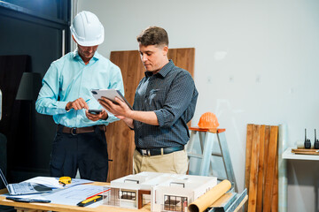 A Caucasian male engineer and an Italian male building contractor are planning and talking at a...
