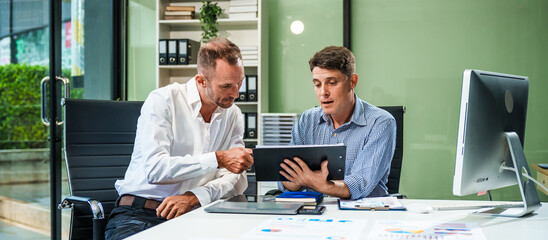 An Italian male and a Caucasian male sit at business desk in office meeting room, discussing...